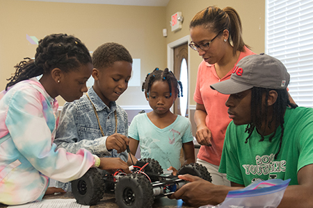 SIUE Noyce intern Gaige Crowell teaches a young student from Alton how to build a rover during the STEM Meets Humanities Robotics Program.